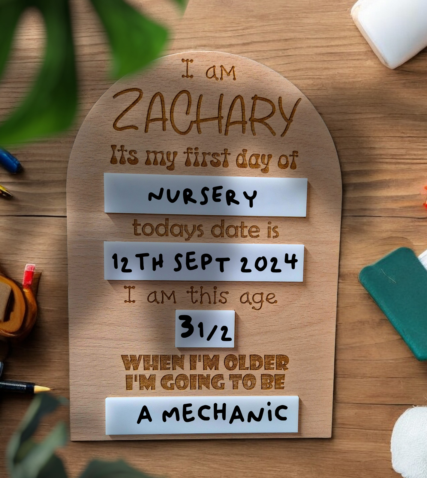 Close-up of engraved name and details on wooden memory board for school or nursery milestones.