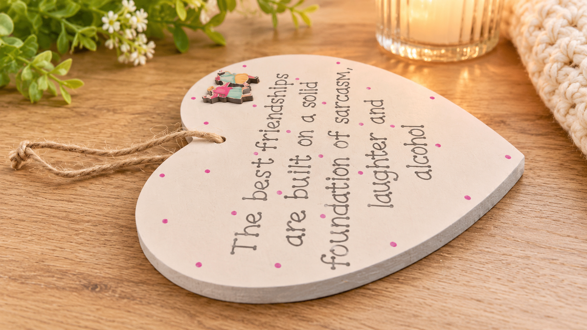 Close-up of the Sarcasm, Laughter and Alcohol friendship wooden heart plaque displayed on a warm wooden tabletop