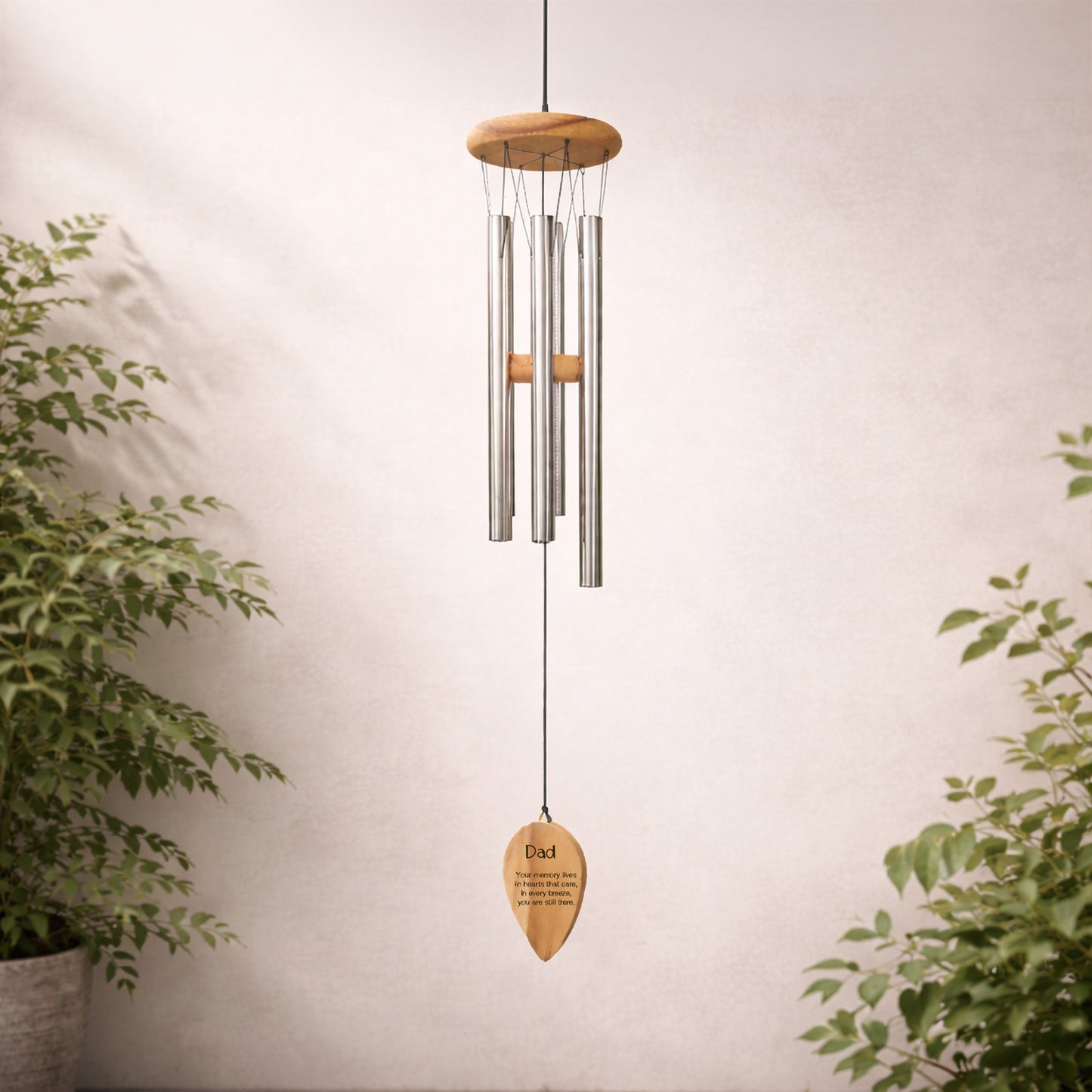 Decorative personalised engraved wind chime with words dad and a quote wooden plaque against a neutral wall with plants.