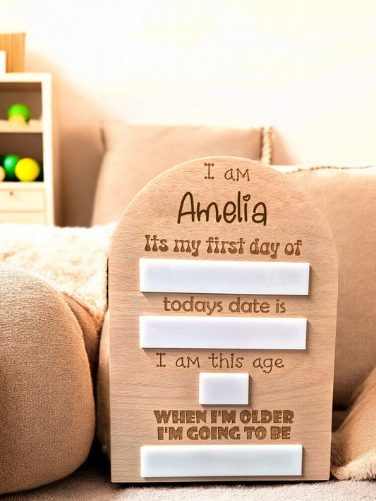 Personalised first day memory board with engraved name and date markers, displayed on a soft fabric surface.