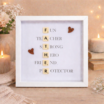 Framed artwork with Scrabble tile letters spelling out FATHER and a message definition of father on a wooden surface.
