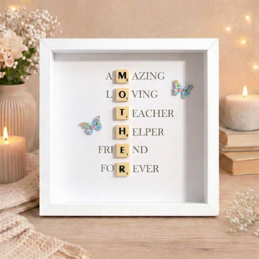 Decorative frame with scrabble letters spelling out  mother and a message of what a mother means on a table with candles and flowers.