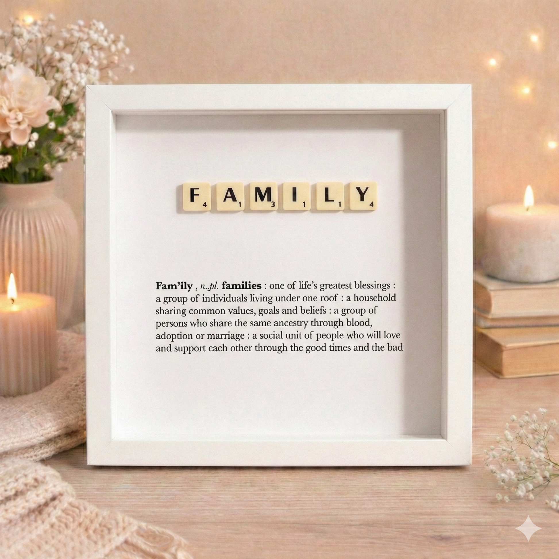 White framed display with 'FAMILY' spelled out using Scrabble tiles on a wooden surface with candles and flowers.