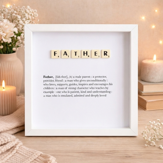 Framed artwork with scrabble tiles spelling 'FATHER' on a wooden surface with candles and flowers.