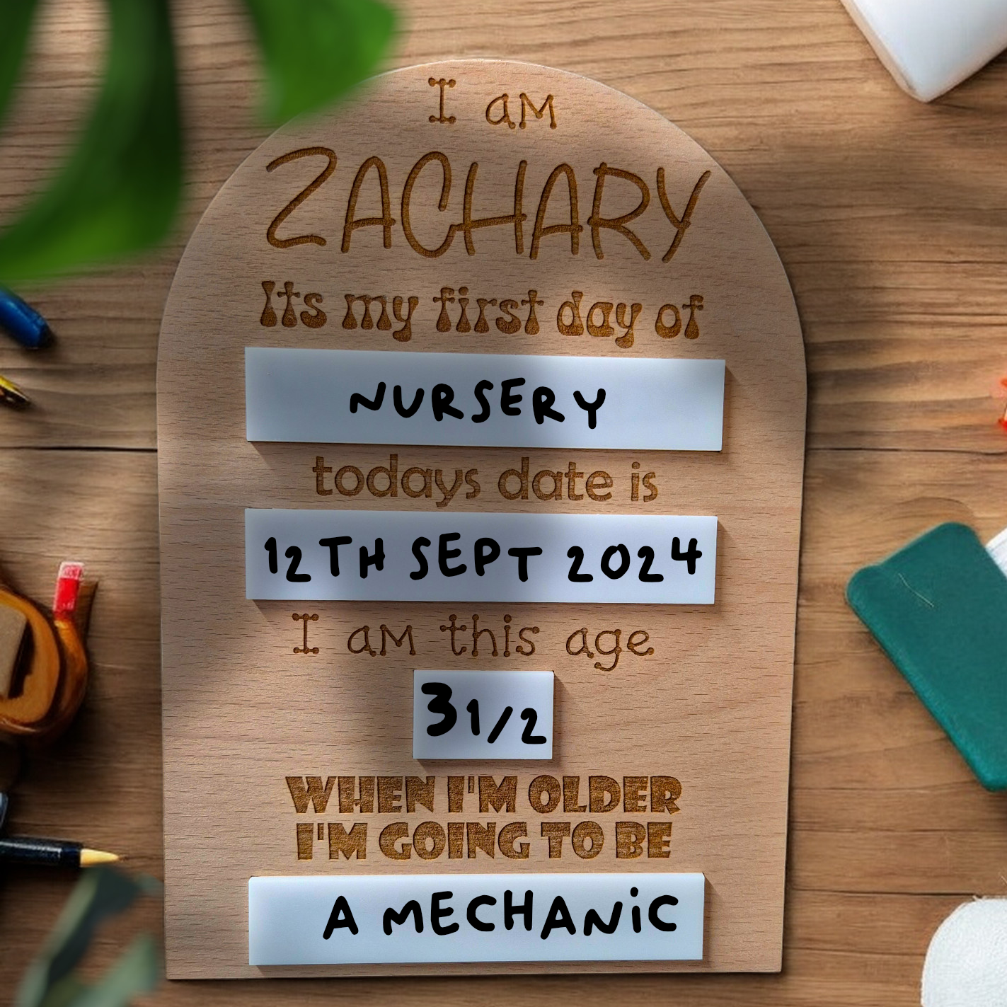 Close-up of engraved name and details on wooden memory board for school or nursery milestones.