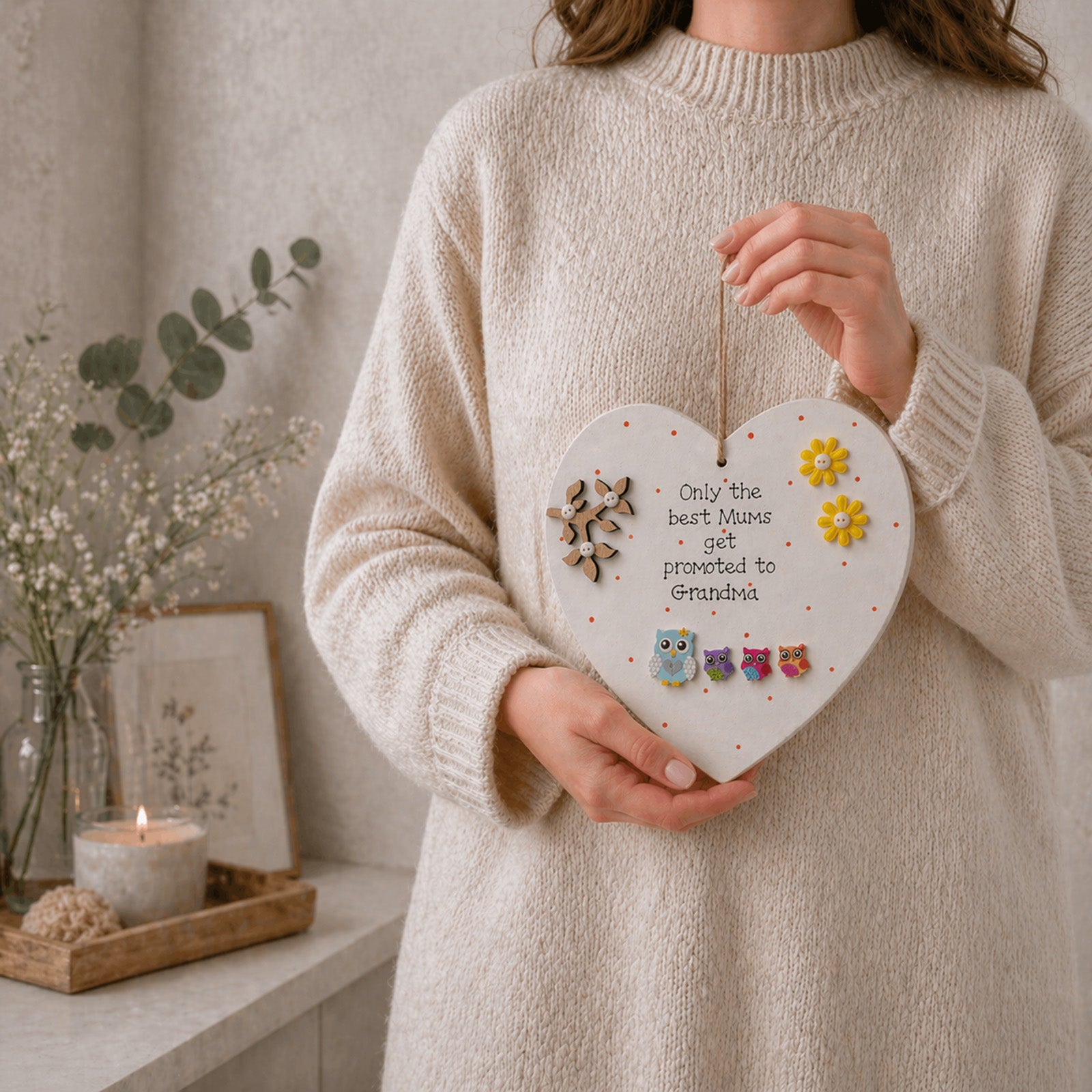 Person holding a heart-shaped decorative plaque with floral designs and only the best mums get promoted to grandma text.