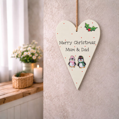 Merry Christmas Mum and Dad wooden heart plaque with Christmas penguins, hanging on a neutral wall