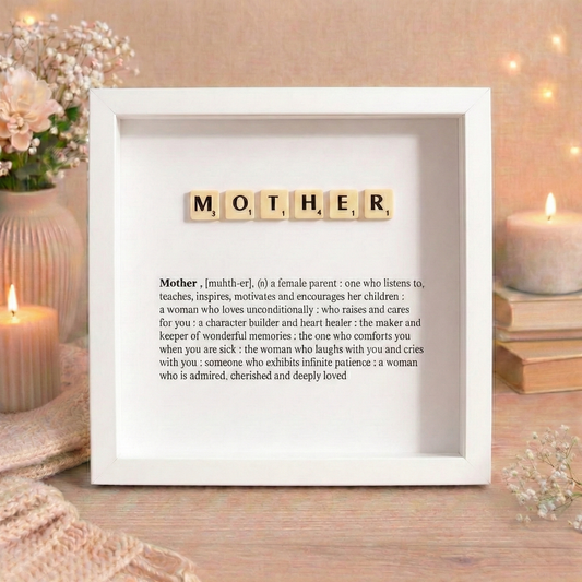 Decorative frame with 'MOTHER' spelled out using Scrabble tiles on a warm-toned background.