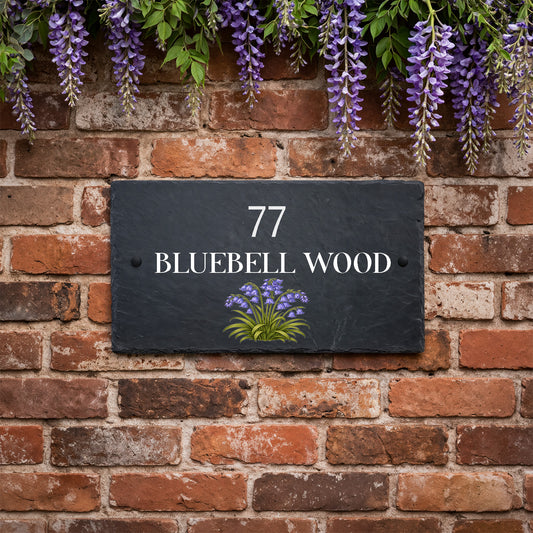 Personalised slate house sign with bluebell design, house number 77 and Bluebell Wood text mounted on a brick wall