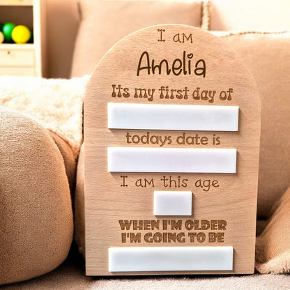 Personalised first day memory board with engraved name and date markers, displayed on a soft fabric surface.