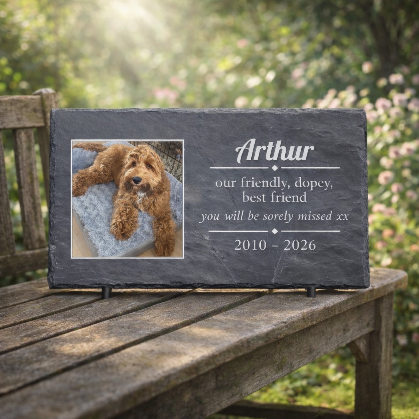 Personalised slate memorial plaque with a photo of a dog and custom text on a wooden table outdoors.