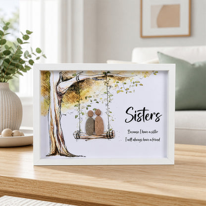 White box frame pebble art showing two stone figures on a tree swing with the quote Sisters Because I have a sister I will always have a friend.