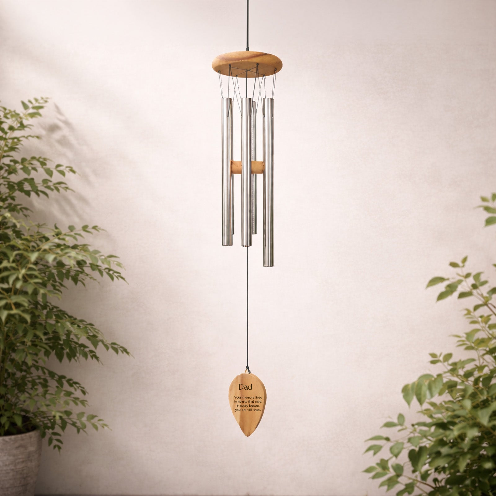 Decorative  personalised engraved wind chime with words dad and a quote wooden plaque against a neutral wall with plants.