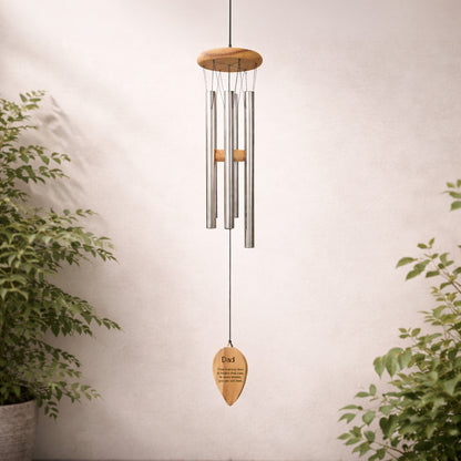 Decorative  personalised engraved wind chime with words dad and a quote wooden plaque against a neutral wall with plants.
