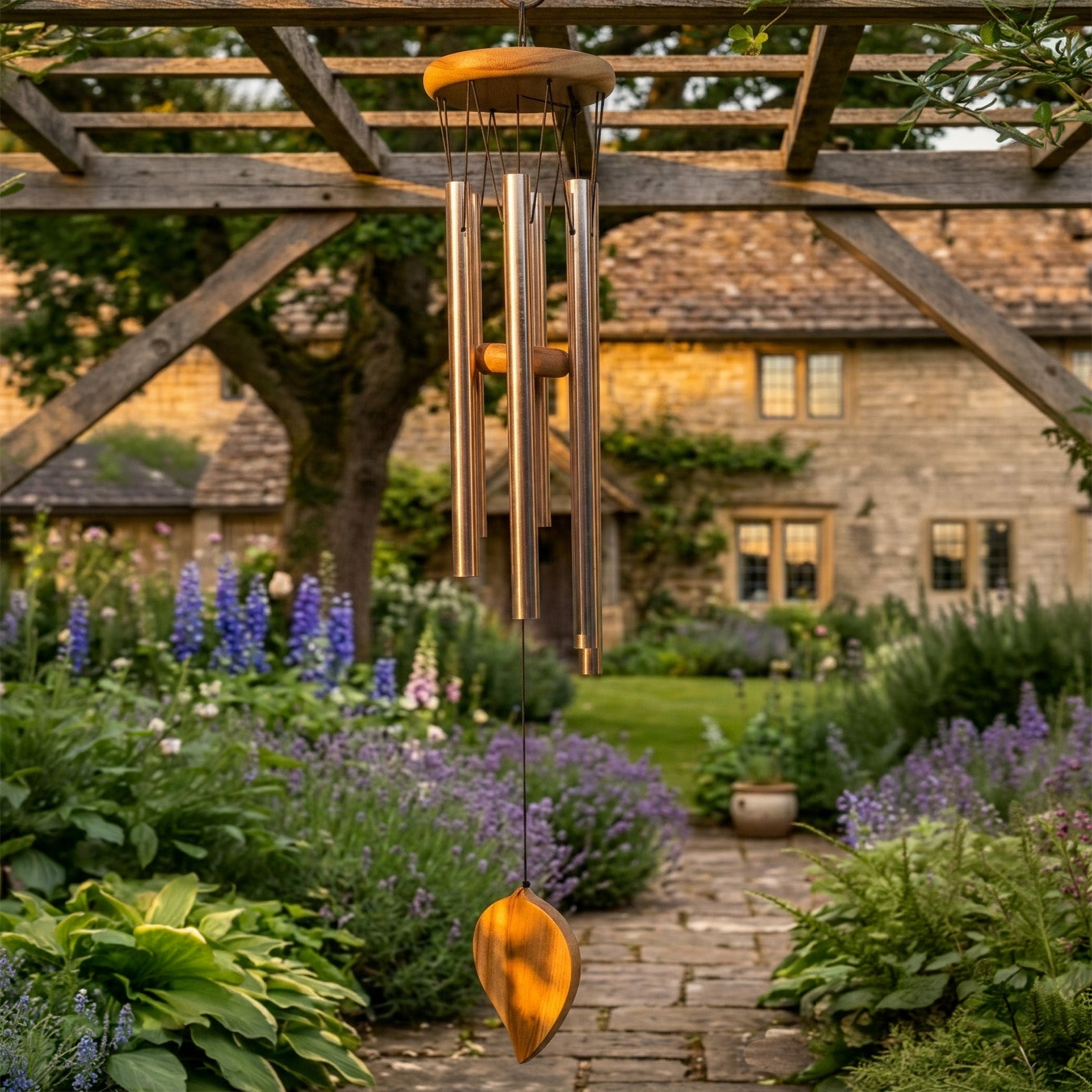 Personalised memorial wind chime hanging from a wooden pergola in a garden with a stone building in the background.